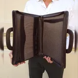 Sobre ejecutivo tamaño oficio de diseño rígido y rectangular. Confeccionado en símil cuero color marrón oscuro con textura veteada. Cuenta con cierre perimetral, manijas integradas y logo de la marca grabado en el frente.