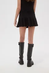 Falda mini tableada de tiro bajo, color negro, con cierre lateral y botón.