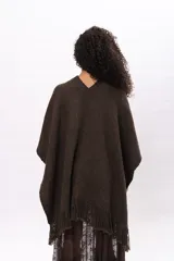 Ruana de tejido de punto color marrón chocolate, con diseño envolvente, cuello en V y detalle de flecos en el ruedo. Incluye etiqueta de cuero sintético con el logo de la marca en la parte frontal.