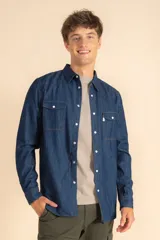 Camisa de jean azul de manga larga, con cierre frontal de botones a presión, dos bolsillos frontales con solapa y costuras reforzadas.