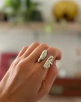 Anillo de diseño orgánico y macizo con forma irregular, elaborado en metal con acabado brillante. Presenta una estructura abierta que permite su ajuste.