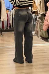 Jean de corte baggy y tiro bajo, color gris con efecto de lavado localizado. Presenta diseño de cinco bolsillos, cierre frontal con botón y cremallera, y pernera ancha.