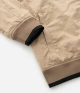 Campera tipo bomber de sarga color beige, con cuello inglés, cierre frontal de cremallera y puños y cintura ajustados con elástico en tono contrastante.
