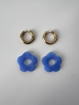 Aros de acero quirúrgico dorados con argollas pequeñas y dijes colgantes en forma de flor color celeste.