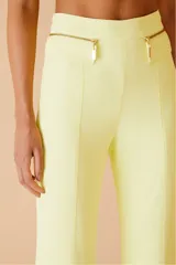 Pantalón amarillo de tiro alto y corte acampanado, con bolsillos frontales con cierre dorado.