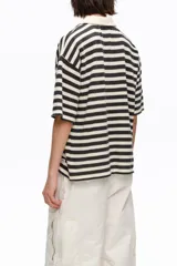 Camiseta a rayas horizontales en negro y blanco, con cuello polo y escote en V con cordones entrelazados. Presenta mangas cortas holgadas y diseño oversize.