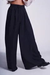 Pantalón negro de corte sastrero con tablas frontales y cintura con lazo. Diseño de pierna ancha y tiro alto.