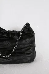 Cartera tipo bolso capitoneada de cuero color negro, con asa de cadena plateada y cuero entrelazado. Forrada por dentro y con bolsillo interno.