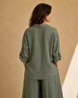 Camisa de lino color verde seco, de corte holgado, con cuello camisero, cierre frontal de botones de nácar, bolsillo aplicado en el pecho y mangas largas con tirilla para sujetar remangadas.