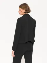 Chaqueta negra con cuello mao y charreteras de cuero ovino tableado en los hombros. Tiene acceso mediante broches forrados de cuero, bolsillos delanteros plaqué con tapa y fuelle, y godet en la espalda baja.