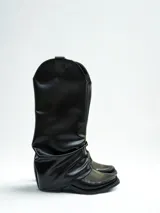 Bota de caña alta color negro, de cuero sintético, con punta cuadrada y efecto arrugado en el tobillo.