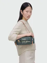 Bolso bandolera Marc Jacobs modelo The Cargo Monogram Denim, con estampado del logo de la marca en azul y verde. Tiene correa de cuero marrón, cierre superior con cremallera, dos bolsillos frontales con hebilla y herrajes dorados.