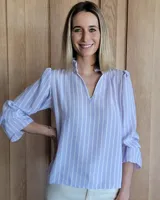 Blusa de algodón con diseño a rayas verticales en tonos lila y blanco. Presenta cuello con detalle de volados, escote en V y mangas tres cuartos con terminación acampanada.