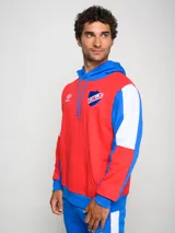 Canguro de felpa Umbro del Club Nacional de Football, con diseño tricolor en rojo, azul y blanco. Presenta capucha con cordones ajustables, bolsillo tipo canguro frontal, logo de la marca y escudo del club bordados en el pecho.