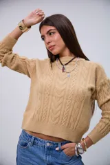 Sweater de punto color beige con cuello redondo, mangas largas y detalles de trenzas en el frente y las mangas.
