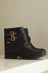 Bota de caña corta negra confeccionada en cuero, con detalle de botamanga y hebillas doradas.