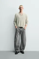 Jeans de denim de algodón en color negro con efecto lavado, corte amplio y silueta curva tipo barrel fit con pinzas en las rodillas. Presenta diseño clásico de cinco bolsillos y cierre frontal con cremallera y botón metálico.