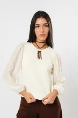 Blusa color manteca de cuello redondo y mangas largas abullonadas con puños elásticos.