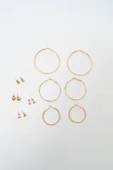 Set de aros dorados compuesto por tres pares de aros tipo argolla de diferentes tamaños y texturas, y cuatro pares de aros pequeños tipo broquel con diseños variados.