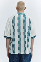 Camiseta de fútbol de manga corta en malla estampada, color blanco con diseño a rayas verticales en tono verde y detalles gráficos en el pecho. Cuenta con cuello abierto verde con finas rayas blancas y corte holgado.