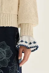 Cardigan de punto color crudo con textura, cuello camisero con borde en contraste, mangas largas con puños acampanados y detalle de bordado floral en la espalda.