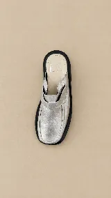 Mocasines destalonados de cuero color plateado, con suela gruesa negra y tira frontal con hebilla decorativa.