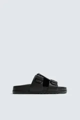 Sandalia tipo slide de goma, color verde militar, con dos tiras anchas ajustables mediante hebillas cuadradas. Presenta plantilla anatómica y suela gruesa con relieve.