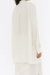 Camisa color crema de corte recto, con cuello camisero con lazada, manga larga y cierre frontal con botonadura.