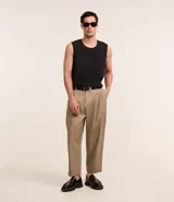 Pantalón de vestir color beige, de corte amplio estilo japonés, con cintura con trabillas, cierre tradicional, pliegues frontales, bolsillos laterales y traseros, y efecto satinado.