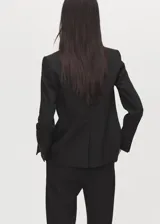 Blazer negro de corte entallado, con cuello de solapa con muesca, hombros estructurados, cierre frontal de un botón, bolsillos de ribete delanteros y manga larga.