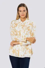 Blusa de manga larga con cuello camisero y cierre frontal de botones. Presenta un diseño estampado en tonos beige y blanco.