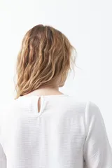 Top negro de manga corta con detalle de nudo en el escote y abertura tipo gota. Presenta una silueta relajada y textura sutil en la tela.