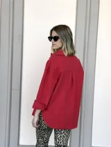 Camisa roja de corte holgado, con cuello clásico, cierre frontal con botones, mangas largas con puños abotonados, dos bolsillos con solapa en el pecho y ruedo recto.