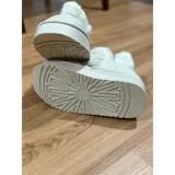 Pantuflas botitas color tostado con diseño acolchado y plataforma, forradas con corderito sintético blanco en el interior y el cuello. Cuentan con una pequeña etiqueta decorativa en el lateral.