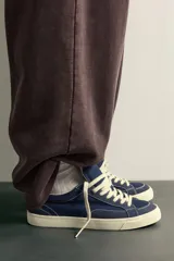 Zapatilla casual de tejido de algodón color beige con detalles en verde y un parche negro en el talón. Cuenta con suela de goma texturizada a contraste.
