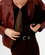 Chaqueta corta color bordó, de manga larga, con cuello camisero, bolsillos frontales con solapa y cierre de botones oscuros.
