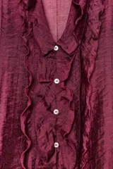 Blusa de escote en pico con volantes decorativos, manga larga con puños elásticos y cierre frontal con botones.