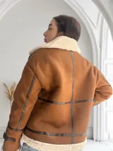 Chaqueta marrón con cuello de piel sintética color crema, cierre frontal con cremallera y hebilla en el cuello, bolsillos laterales con ribete de cuero marrón y puños con ribete de piel sintética.