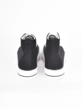 Zapatilla de caña alta con plataforma, confeccionada en lona negra con cordones y puntera de goma blanca.