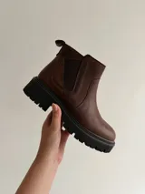 Bota corta de cuero color marrón con suela track dentada y cierre lateral.