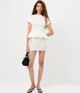 Blusa de punto Roma color celeste, con cuello alto, mangas cortas y diseño peplum. Presenta recortes estructurales y un cinturón integrado con hebilla metálica en la cintura, finalizando en un ruedo con volados.