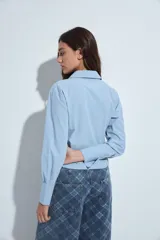 Camisa blanca de manga larga con cuello clásico y cierre frontal de botones. Presenta un diseño entallado con frunces decorativos en la parte central delantera.