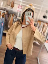 Chaqueta corta de textura efecto ante en color beige, con diseño abierto, cuello redondo y bolsillos frontales. Presenta costuras horizontales decorativas y mangas largas.