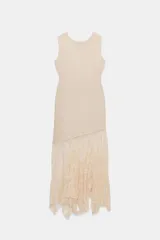 Vestido midi de color beige, con cuello redondo y diseño sin mangas. Presenta un cuerpo liso de punto con bajo asimétrico y una falda inferior confeccionada en encaje tono sobre tono.