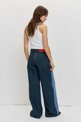 Jean wide leg de tiro medio, confeccionado en denim azul con detalles de paneles laterales en un tono más oscuro, tiro medio, cierre frontal con botón y cremallera, y diseño de perneras amplias.