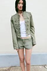 Short mini de tiro bajo color verde oliva, con detalle de botones metálicos y aplicaciones decorativas en el mismo tejido. Cuenta con cierre frontal oculto.
