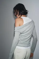 Camiseta de manga larga gris melange con cuello redondo y diseño asimétrico que simula una doble camiseta, con una capa inferior blanca visible en el cuello y el bajo.