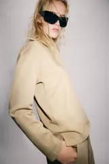 Polo oversize de algodón color beige, de manga larga, con cuello camisero y cierre frontal de botones ocultos.