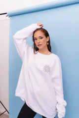 Buzo oversize de cuello redondo en color blanco, con estampa gráfica en la espalda que incluye motivos uruguayos, el sol, la bandera, un jugador de fútbol y elementos tradicionales.