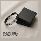 Pulsera de diseño masculino con placa central de acero inoxidable que presenta un grabado de una mano de Hamsa. La estructura se complementa con una banda de goma negra, ofreciendo un estilo moderno y resistente.